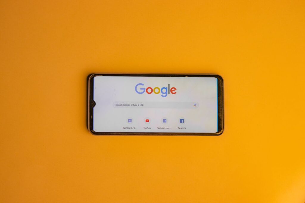 Smartphone displaying Google search page on a vibrant yellow background.